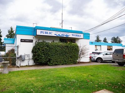 White building with blue trim around the top and a sign with the City of Nanaimo logo and "Public Works"
